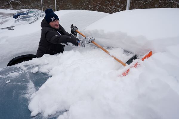 Cary Fallath, the BMW Store lot technician, clears snow from new cars in Silverton, Ohio, Tuesday, Jan. 7, 2025. (AP Photo/Carolyn Kaster)