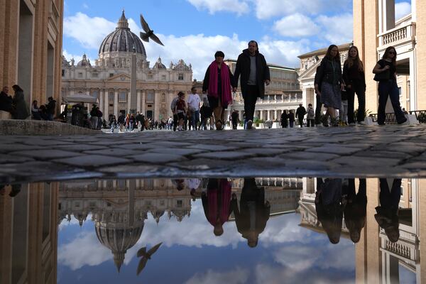 People are reflected in a puddle as they walk in in front of St. Peter's Square at the Vatican, Thursday, Feb. 27, 2025. (AP Photo/Alessandra Tarantino)