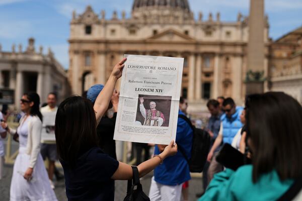 Tourists take photographs with a L'Osservatore Romano newspaper with the image of Pope Leo XIV at the Vatican, Friday, May 9, 2025, a day after he was elected history's first North American pope. (AP Photo/Francisco Seco)