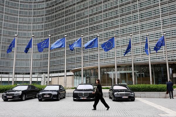 European Union flags flap in the wind as a woman walks past diplomatic vehicles outside of EU headquarters in Brussels, Belgium, Tuesday, May 27, 2025. (AP Photo/Omar Havana)