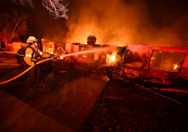 A firefighter from Costa Mesa works to extinguish a fire burning a home on Valleylights Drive during the Eaton fire in the Hastings Ranch community of Pasadena, Calif., early Wednesday, Jan. 8, 2025. (Will Lester/The Orange County Register via AP)