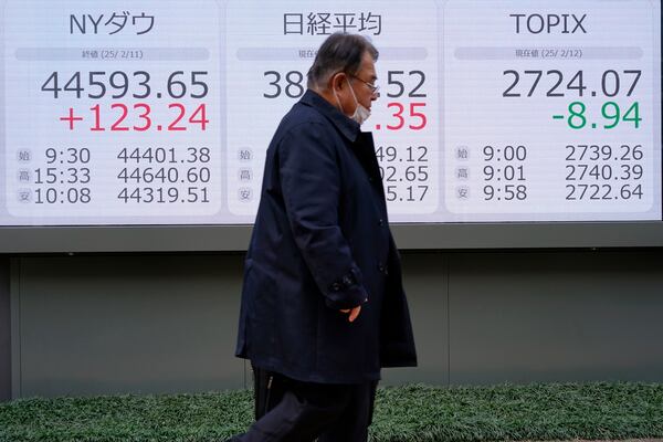 FILE - A person walks in front of an electronic stock board showing New York Dow, Japan's Nikkei and TOPIX indexes at a securities firm Wednesday, Feb. 12, 2025, in Tokyo. (AP Photo/Eugene Hoshiko, File)