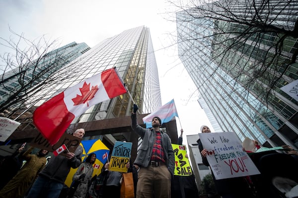 People wave flags and hold signs during a protest outside of the U.S embassy in Vancouver, British Columbia, Tuesday, March 4, 2025. (Ethan Cairns/The Canadian Press via AP)