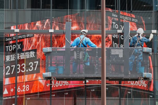 Workers clean the glass window of a building in front of an electronic stock board showing Japan's TOPIX index at a securities firm Friday, May 23, 2025, in Tokyo. (AP Photo/Eugene Hoshiko)
