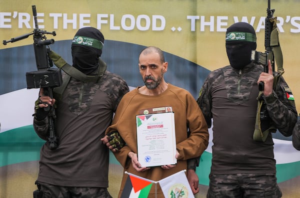 Israeli captive, Eli Sharabi, who has been held hostage by Hamas in Gaza since October 7, 2023, stands on a stage escorted by Hamas fighters before being handed over to the Red Cross in Deir al-Balah, central Gaza Strip, Saturday Feb. 8, 2025. (AP Photo/Abdel Kareem Hana)