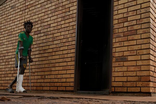 Lucky Mbizana walks on crutches outside his parents' home in Stilfontein, South Africa, Wednesday, Jan. 15, 2025. (AP Photo/Themba Hadebe)