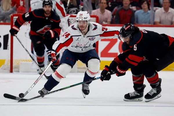 Washington Capitals' Connor McMichael (24) tries to chip the puck past Carolina Hurricanes' Jalen Chatfield (5) during the first period of Game 3 of an NHL hockey Semi-final round playoff series in Raleigh, N.C., Saturday, May 10, 2025. (AP Photo/Karl DeBlaker)