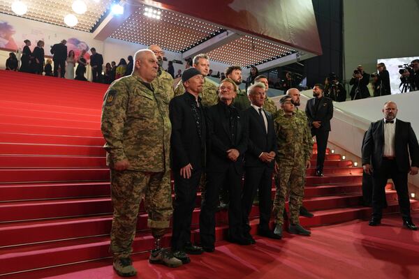 The Edge, from second left, Bono and Sean Penn pose with military personnel for photographers upon arrival at the premiere of the film 'Bono: Stories of Surrender' at the 78th international film festival, Cannes, southern France, Friday, May 16, 2025. (AP Photo/Natacha Pisarenko)