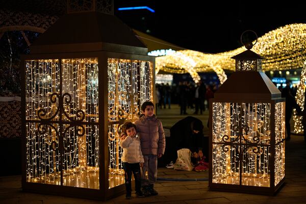 Children pose for a picture next to the lighting decorations in a square on the first day of the Muslim holy month of Ramadan in Istanbul, Turkey, Saturday, March 1, 2025. (AP Photo/Khalil Hamra)