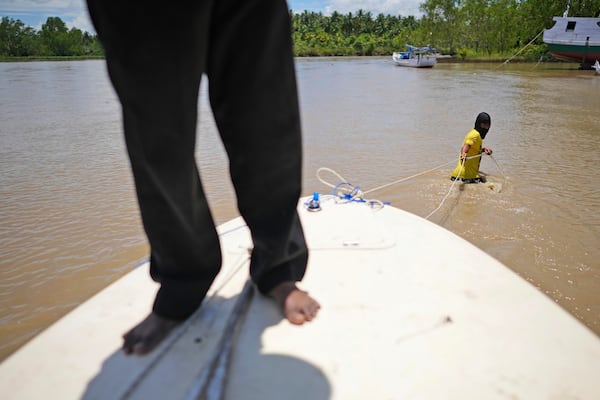 A man walks in the water as he pulls his boat to the riverbank in Budong-Budong, Sulawesi Island, Indonesia, Tuesday, Feb. 25, 2025. (AP Photo/Dita Alangkara)