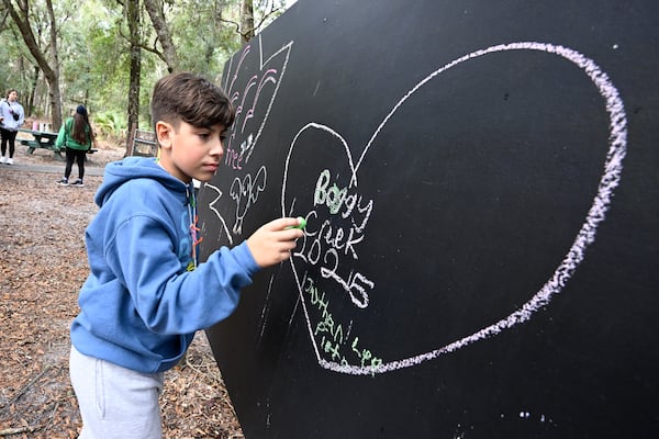 A child writes on a blackboard at Camp Boggy Creek, where children with serious illnesses and their families are provided with a free camp experience, Saturday, Jan. 11, 2025, in Eustis, Fla. (AP Photo/Phelan M. Ebenhack)