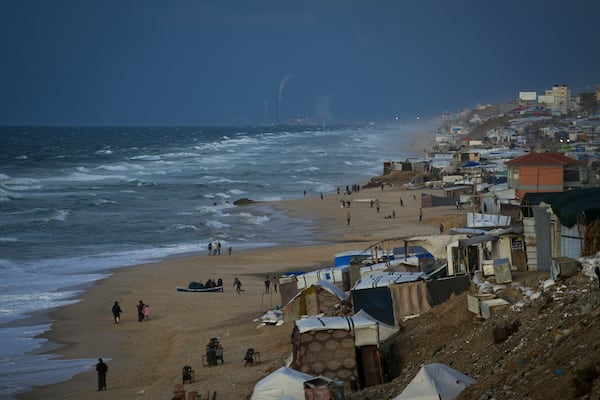 People walk along the beach next to a tent refugee camp for displaced Palestinians in Deir al-Balah, central Gaza Strip, Monday, Dec .30, 2024. (AP Photo/Abdel Kareem Hana)