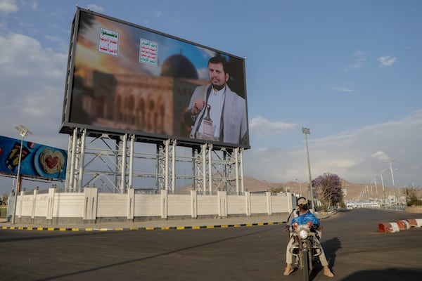 Yemenis pass under a street billboard displaying a picture of Abdul Malik al-Houthi, the leader of the Houthi movement, in Sanaa, Yemen, Tuesday, March 18, 2025. Arabic reads, "death to America, death to Israel". (AP Photo/Osamah Abdulrahman)