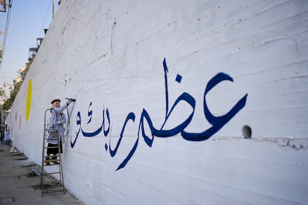 A girl writes "Worship your God" in Arabic as a group of young volunteers paints a mural symbolizing peace on a wall on the outskirts of Damascus, Syria, Sunday Jan. 12, 2025. (AP Photo/Mosa'ab Elshamy)