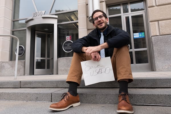 A United States Agency for International Development, or USAID, contract worker sits in front of the USAID office with a message written on a piece of paper, Monday, Feb. 3, 2025, in Washington (AP Photo/Manuel Balce Ceneta)