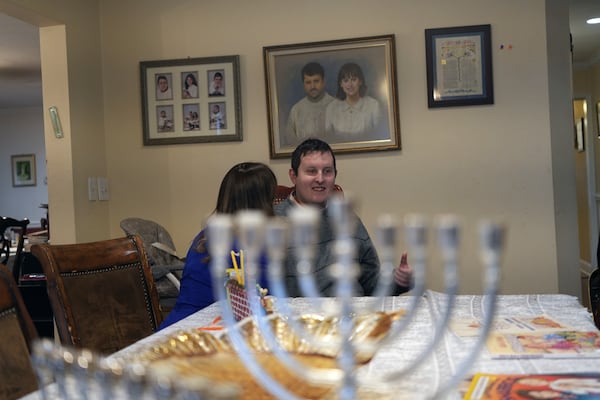 Dov Marcus talks to his mother, Debbie Marcus, at their dining table near the branched candelabra called a menorah, in Teaneck, N.J., on Friday, Dec. 20, 2024. (AP Photo/Luis Andres Henao)