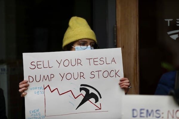 FILE - A person protesting Elon Musk's actions in the Trump administration holds a sign outside a Tesla showroom in Seattle on Thursday, Feb. 13, 2025. (AP Photo/Manuel Valdes, File)