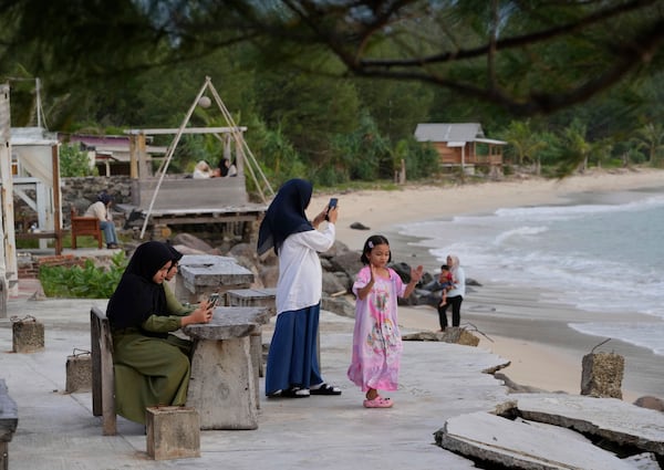 Young girls use their mobile phones as they visit Lampuuk beach, one of the areas hardest hit by Indian Ocean tsunami in 2004, on the outskirts of Banda Aceh, Indonesia, Friday, Dec. 13, 2024. (AP Photo/Achmad Ibrahim)