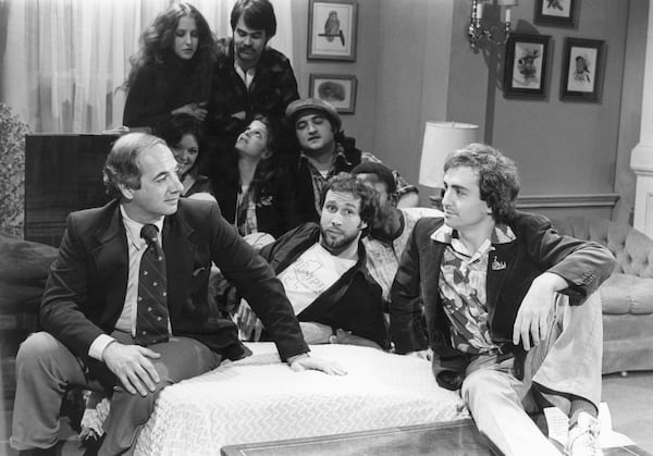 FILE - White House Press Secretary Ron Nessen, left, appears on the "Saturday Night Live" set with producer Lorne Michaels, right, and cast members Chevy Chase, foreground center, Laraine Newman, background left, Dan Aykroyd, background right, Jane Curtin, second row from left, Gilda Radner, John Belushi and Garret Morris, partially obscured, on April 17, 1976, in New York. Nessen, a veteran broadcast journalist who served as press secretary for President Gerald Ford, died March 12, 2025. He was 90. (AP Photo, File)