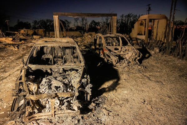 Charred vehicles are illuminated by utility lights at homes destroyed by the Palisades Fire in the Pacific Palisades neighborhood of Los Angeles, Thursday, Jan. 16, 2025. (AP Photo/Damian Dovarganes)