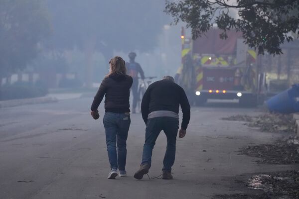 People walk along a street after the Palisades Fire ravaged a neighborhood amid high winds in the Pacific Palisades neighborhood of Los Angeles, Thursday, Jan. 9, 2025. (AP Photo/Damian Dovarganes)