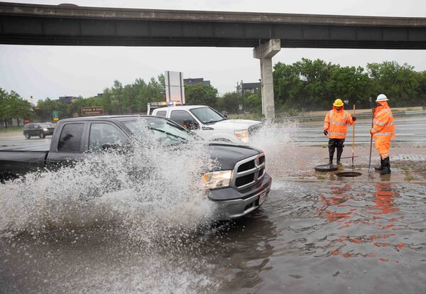 A pick-up truck passes as Tristan Neal, and Kirk Jackson with TxDOT work to clear a clogged sewer drain that caused a N Central Expressway frontage road to flood in Dallas, Wednesday, April 30, 2025. (Juan Figueroa/The Dallas Morning News via AP)
