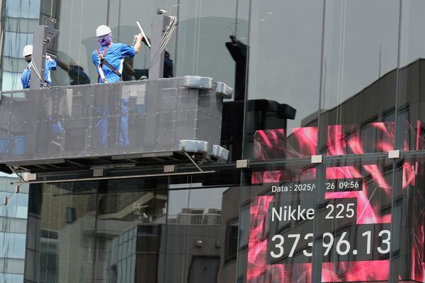 Workers clean the glass window of a building in front of an electronic stock board showing Japan's Nikkei index at a securities firm Monday, May 26, 2025, in Tokyo. (AP Photo/Eugene Hoshiko)