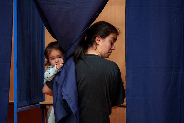 A woman holds a baby as she casts her vote inside a voting booth in the first round of the presidential election redo in Bucharest, Romania, Sunday, May 4, 2025. (AP Photo/Andreea Alexandru)
