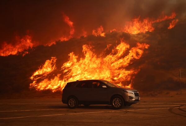 A vehicle rides past a hillside engulfed in flames caused by the Hughes Fire in Castaic, Calf., Wednesday, Jan. 22, 2025. (AP Photo/Ethan Swope)