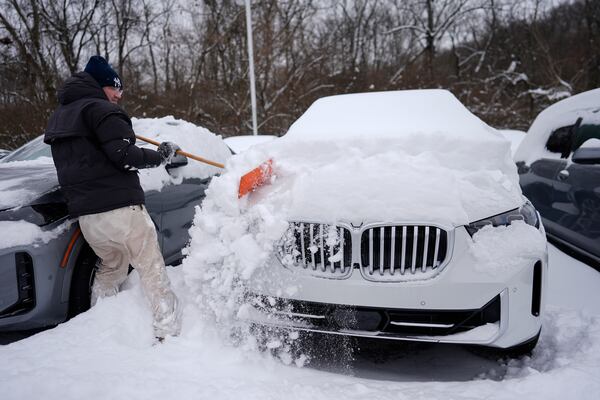 Cary Fallath, the BMW Store lot technician, clears snow from new cars in Silverton, Ohio, Tuesday, Jan. 7, 2025. (AP Photo/Carolyn Kaster)