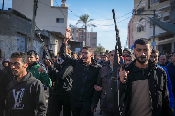 Relatives and neighbors, two of them holding guns, walk during the funeral procession of a victim of an Israeli strike on a home late Saturday that killed at least eight people, in Deir al-Balah, central Gaza Strip, Sunday, Dec. 22, 2024. Some families in Gaza are armed to protect their homes from thieves in the camps.(AP Photo/Abdel Kareem Hana)