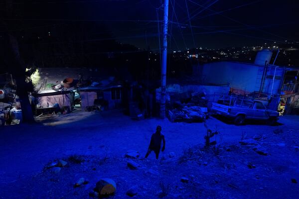 Cuban migrant Dayron Garcia Jr, is bathed in blue light from a streetlight in front of Martha Rosales' home, where his family is staying while waiting an appointment to apply for asylum in the United States through the CBP One app Wednesday, Aug. 28, 2024, in Tijuana, Mexico. (AP Photo/Gregory Bull)