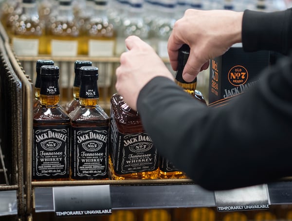 A B.C. Liquor Store employee demonstrates removing bottles of American whiskey for media before a news conference in Vancouver, B.C., Sunday, Feb. 2, 2025. (Ethan Cairns/The Canadian Press via AP)