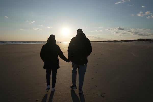 Susan and Greg Scarbro hold hands while walking on the beach at sunset in Sunset Beach, N.C. on Jan. 3, 2025. (AP Photo/Laura Bargfeld)