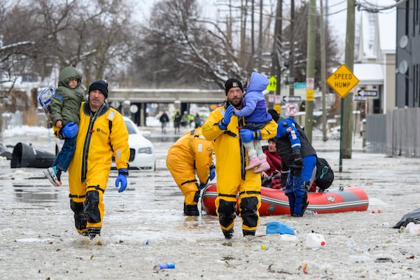 Members of the Downriver Dive Team carry children to safety after a water main break in Detroit caused massive flooding, triggering evacuations, Monday, Feb. 17, 2025. (Andy Morrison/Detroit News via AP)