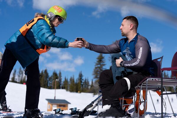 A worker with Oregon Adaptive Sports hands Ukrainian veteran Oleksandr Shvachka a cup of water during a break in a lesson on the three track skiing method at Hoodoo Ski Area in central Oregon on Thursday, March 6, 2025. (AP Photo/Jenny Kane)