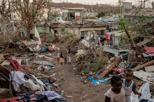 A family stands in the middle of wreaked houses in Mamoudzou, Mayotte, Thursday, Dec. 19, 2024 (AP Photo/Adrienne Surprenant)