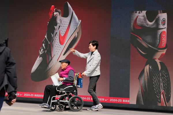 A woman pushes an elderly man past a Nike store at a mall in Beijing, Wednesday, May 7, 2025. (AP Photo/Ng Han Guan)