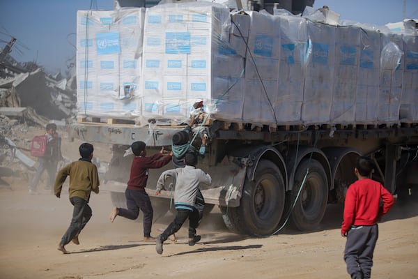 Palestinians chase humanitarian aid trucks that arrived through the Kerem Shalom crossing from Egypt into the Gaza Strip, in Rafah, Tuesday, Jan. 21, 2025. (AP Photo/Jehad Alshrafi)