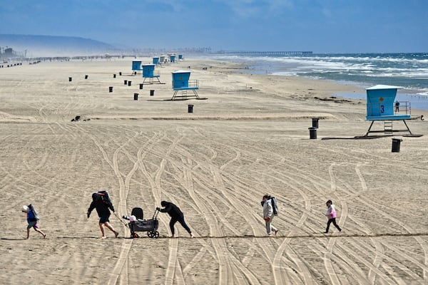 Beach goers trudge through the sand in a windy day south of the pier in Huntington Beach, Calif., Thursday, March 13, 2025, after strong storms moved through the region overnight. (Jeff Gritchen/The Orange County Register via AP)