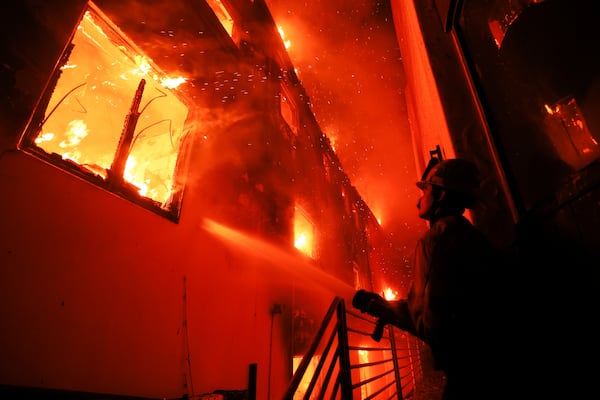 A firefighter works from a deck as the Palisades Fire burns a beachfront property Wednesday, Jan. 8, 2025, in Malibu, Calif. (AP Photo/Etienne Laurent)