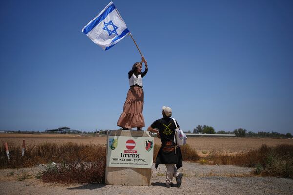 An activist stands on a concrete block signaling border ahead as she waves an Israeli flag towards trucks loaded with humanitarian aid for the Gaza Strip in southern Israel, Wednesday, May 21, 2025. (AP Photo/Ohad Zwigenberg)