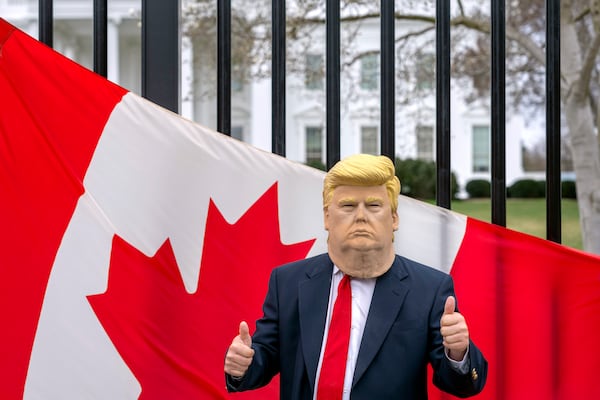 A visitor to the city wearing a mask of President Donald Trump poses for a photo in front of a Canadian flag being held by tourists from Toronto showing their support for Canada regarding trade tariffs, in front of the White House in Washington, Thursday, March 13, 2025. (AP Photo/Ben Curtis)