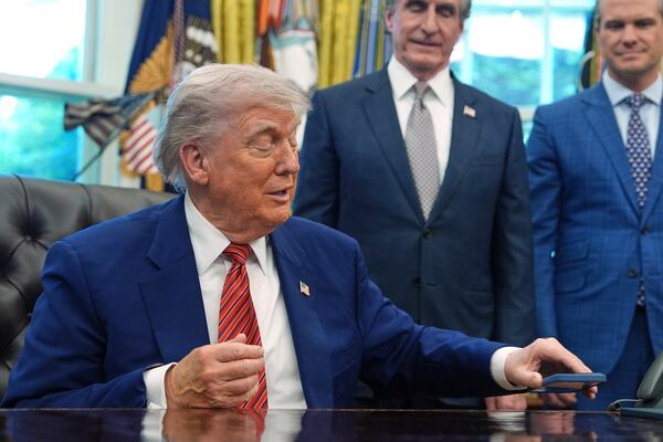 President Donald Trump silences his mobile phone which rang two times as he was speaking to reporters after signing executive orders regarding nuclear energy in the Oval Office of the White House, Friday, May 23, 2025, in Washington. (AP Photo/Evan Vucci)