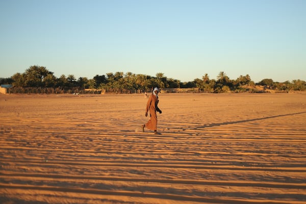 A man walks through sand with palm trees in the distance in Chinguetti, Mauritania on Feb. 3, 2025. (AP Photo/Khaled Moulay)