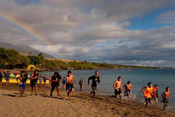 Members of the Napili Canoe Club run on the beach as a rainbow forms nearby on Monday, July 8, 2024, at Hanakao'o Park in Lahaina, Hawaii. (AP Photo/Lindsey Wasson)