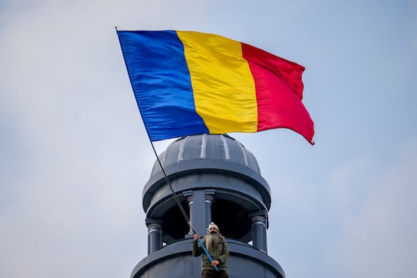 A man perched on the roof of a building waves the Romanian flag during a rally organized by the right wing Alliance for the Unity of Romanians (AUR), calling for free elections after Romania' s Constitutional Court annulled the first round of presidential elections last December, in Bucharest, Romania, Sunday, Jan. 12, 2025. (AP Photo/Vadim Ghirda)