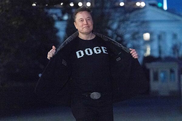 Elon Musk flashes his t-shirt that reads "DOGE" to the media as he walks on South Lawn of the White House, in Washington, Sunday, March 9, 2025. (AP Photo/Jose Luis Magana)