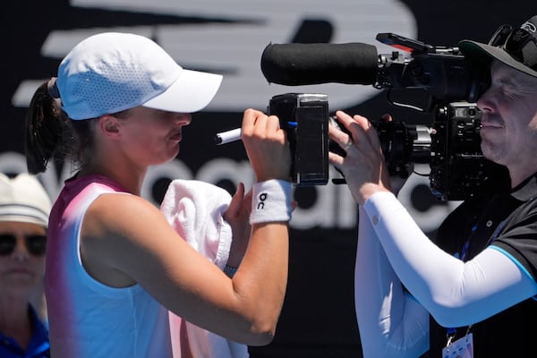 Iga Swiatek of Poland signs a screen on a television camera after defeating Emma Raducanu of Britain in their third round match at the Australian Open tennis championship in Melbourne, Australia, Saturday, Jan. 18, 2025. (AP Photo/Asanka Brendon Ratnayake)