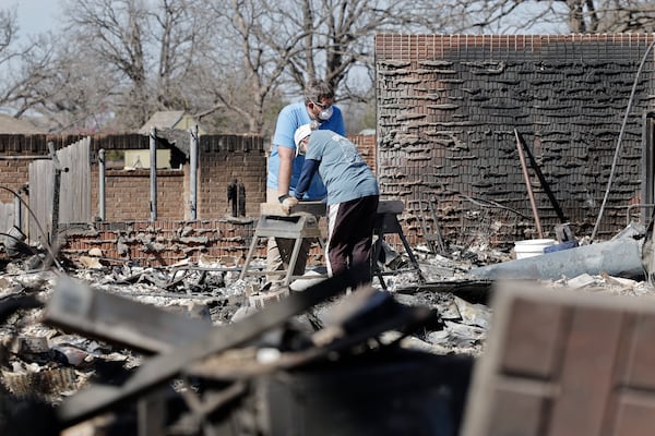 Cayton Jones, left, and his family look through the ashes of his home in the Hidden Oaks neighborhood in Stillwater, Okla., Monday, March 17, 2025, after wildfires burned through the area on Friday. (AP Photo/Alonzo Adams)